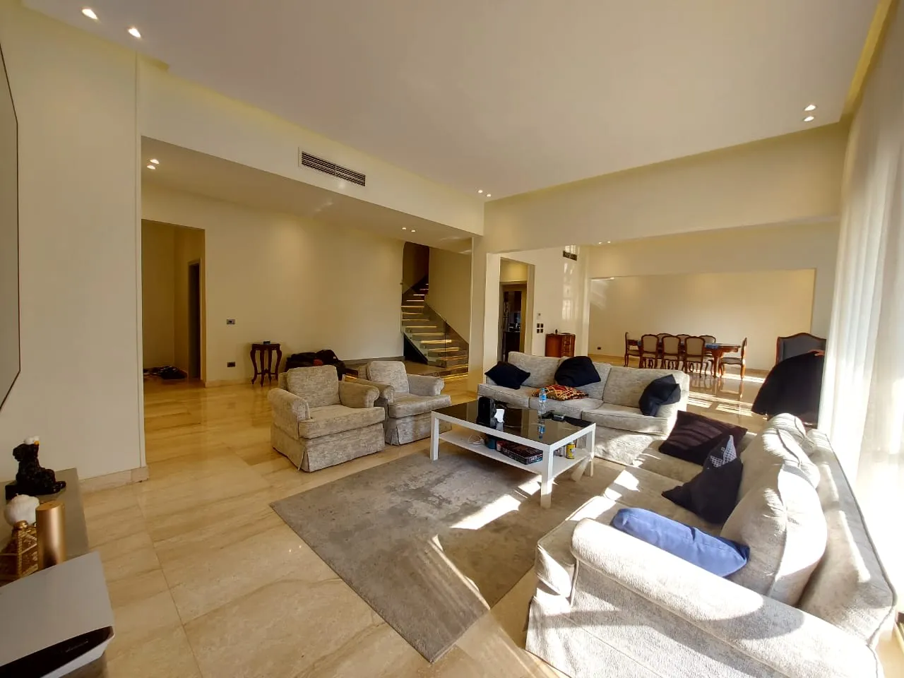 Sunlit living room of a duplex for sale in Zamalek, Cairo with beige sofas and the internal staircase behind