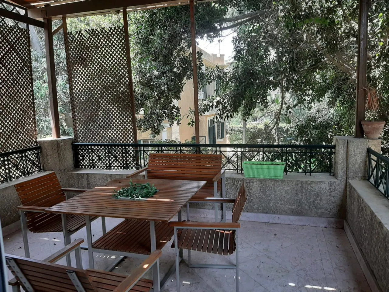 Shaded terrace with a wooden dining set and lattice screens over the trees at a penthouse in Sarayat, Maadi