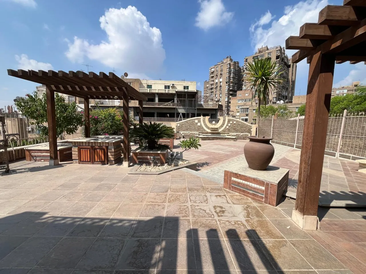 Large paved roof terrace with a wooden pergola and planters at a penthouse in Zamalek, Cairo