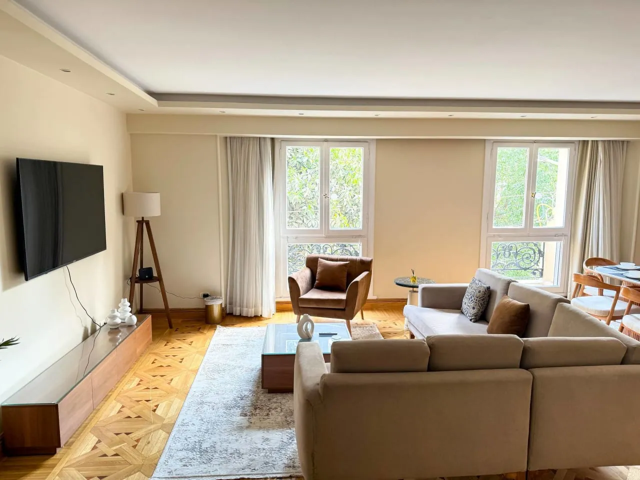 Furnished living room with a beige sectional sofa, parquet floor and wall TV in a serviced apartment in Heliopolis