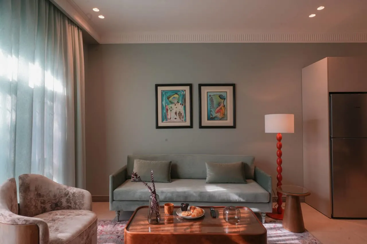 Furnished living room with a grey sofa, velvet armchair and framed prints in a serviced apartment in Maadi, Cairo