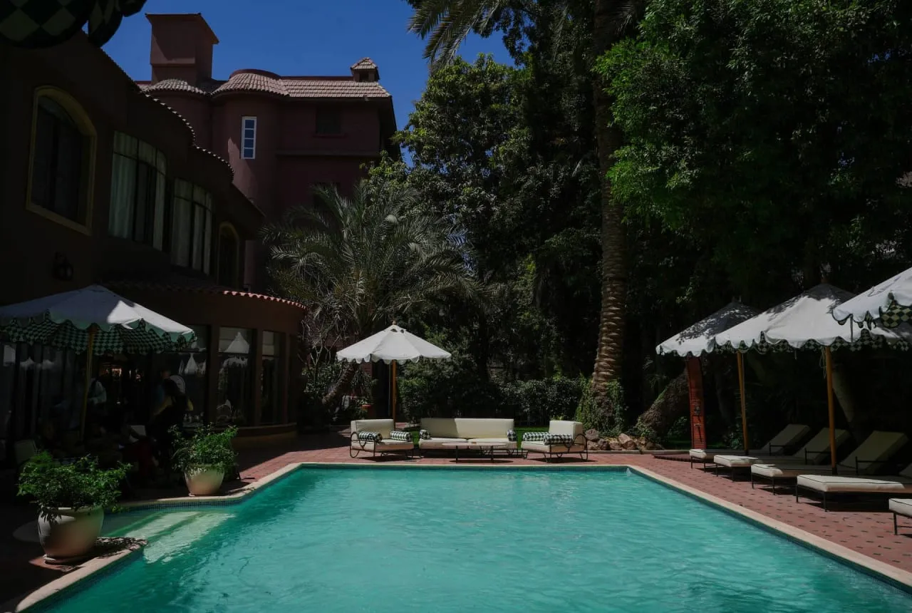 Swimming pool with white parasols and sun loungers beside a leafy garden at a serviced apartment building in Maadi