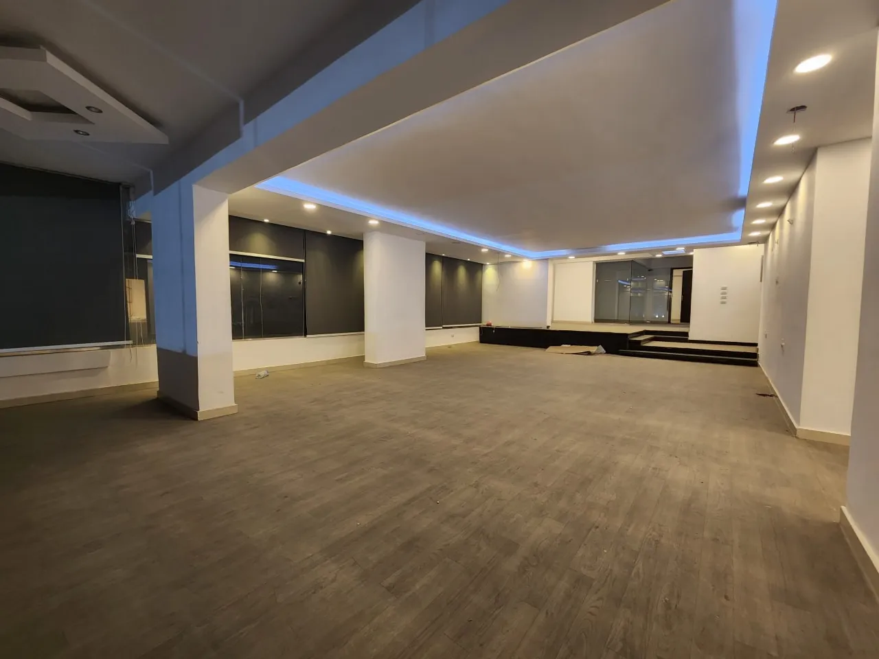 Empty showroom with wood-look flooring, columns and blue cove lighting in a shop in Zahraa El Maadi