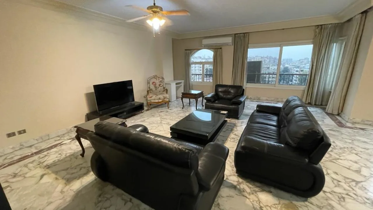Marble-floored sitting room with black leather sofas and a city view, in a furnished apartment for rent in Degla