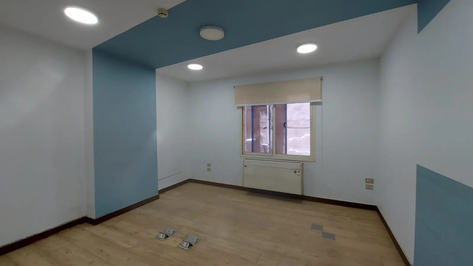 Room on a full floor in Degla lit by recessed downlights, with a painted accent wall and a window