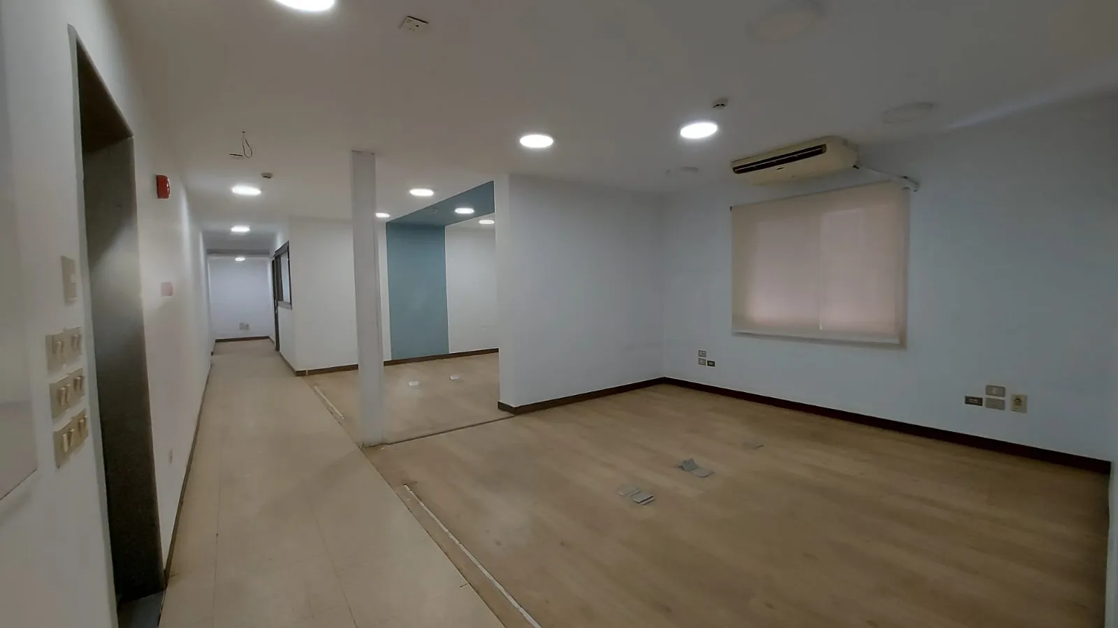 Open span of an empty full floor in Degla seen through a doorway, with downlights and a window at the far end
