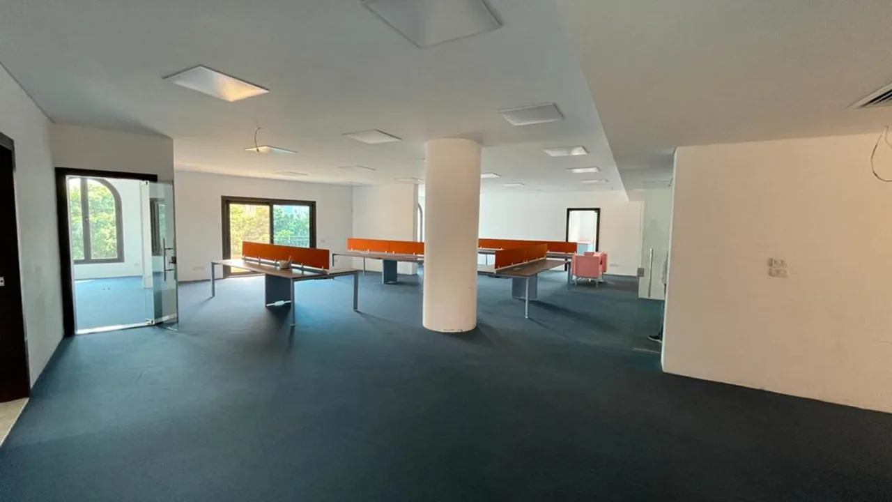 Open-plan floor with bench desks, a structural column and arched windows, in an administrative office for rent in Degla