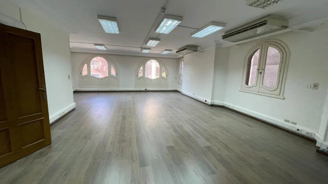 Empty office floor with laminate flooring, ceiling panel lights and three arched windows, in an office for rent in Degla
