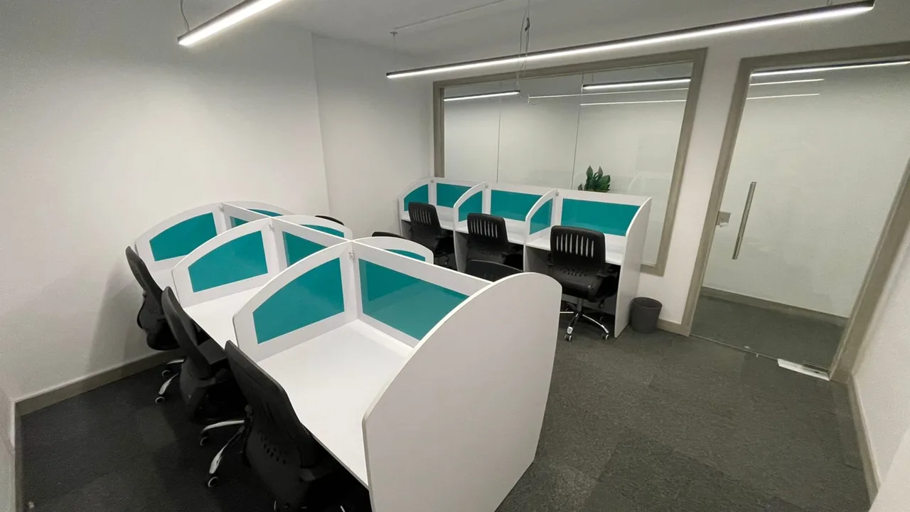 White workstations with teal screens behind a glass partition, in an administrative office for rent in Degla