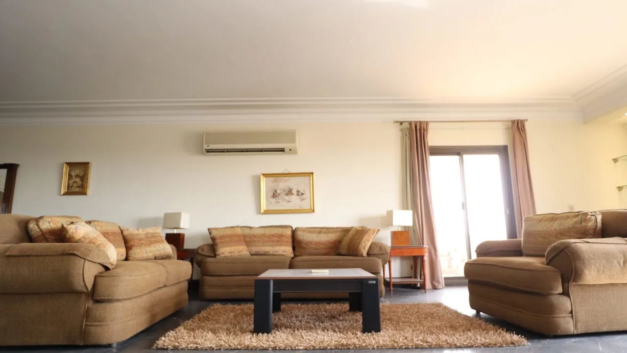 Furnished reception with deep sofas on a marble floor and curtained windows on two sides, in a penthouse for sale in Degla