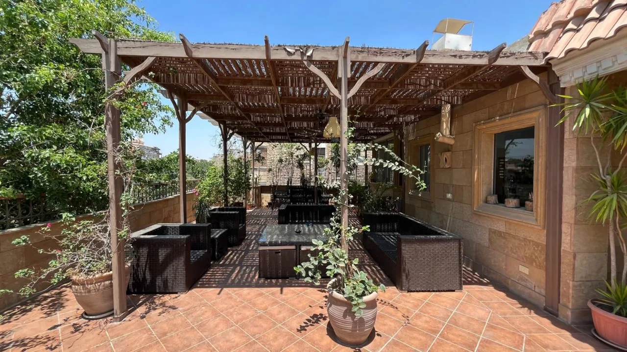 Roof terrace under a timber pergola with rattan seating and treetop views, at a penthouse for rent in Degla