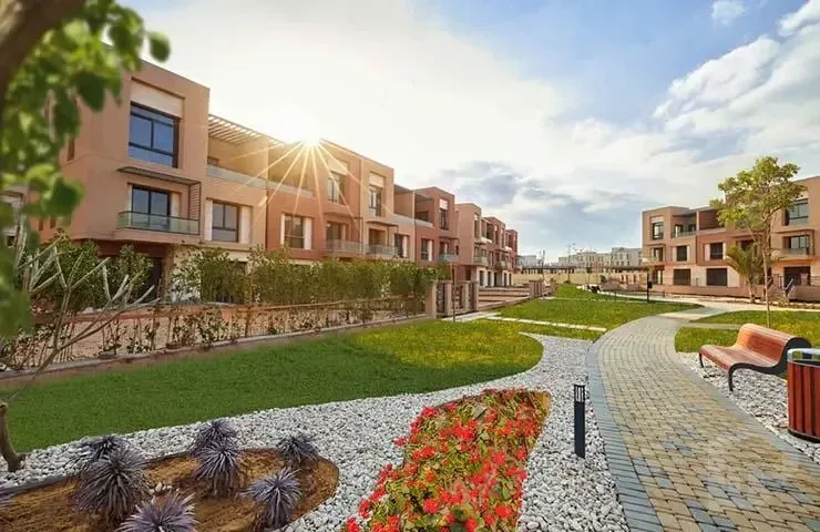 مبانٍ سكنية بلون الطوب وبلكونات على ممر حديقة منسقة في ديستريكت 5 بالقاهرة الجديدة