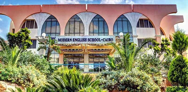 الواجهة المقوّسة لمدرسة Modern English School Cairo في القاهرة الجديدة خلف النخيل والحدائق