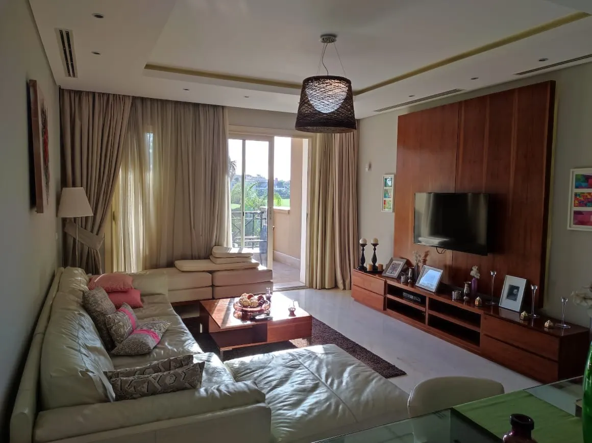 Furnished living room of an apartment in Fifth Settlement, New Cairo with leather sofas and a wood-panelled TV wall