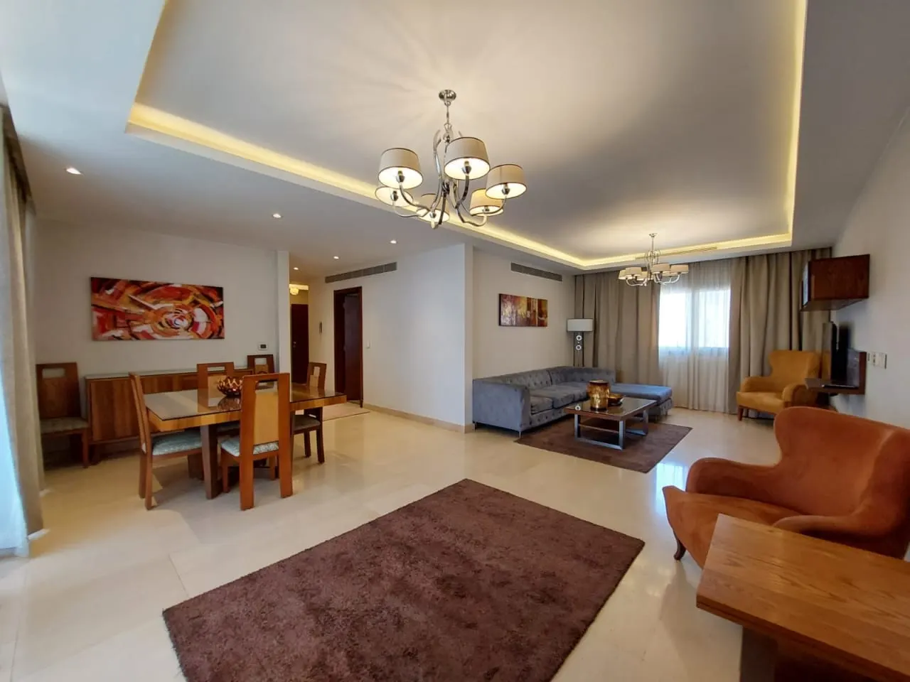 Furnished living and dining room of an apartment for rent in New Cairo with an orange armchair and wooden dining set