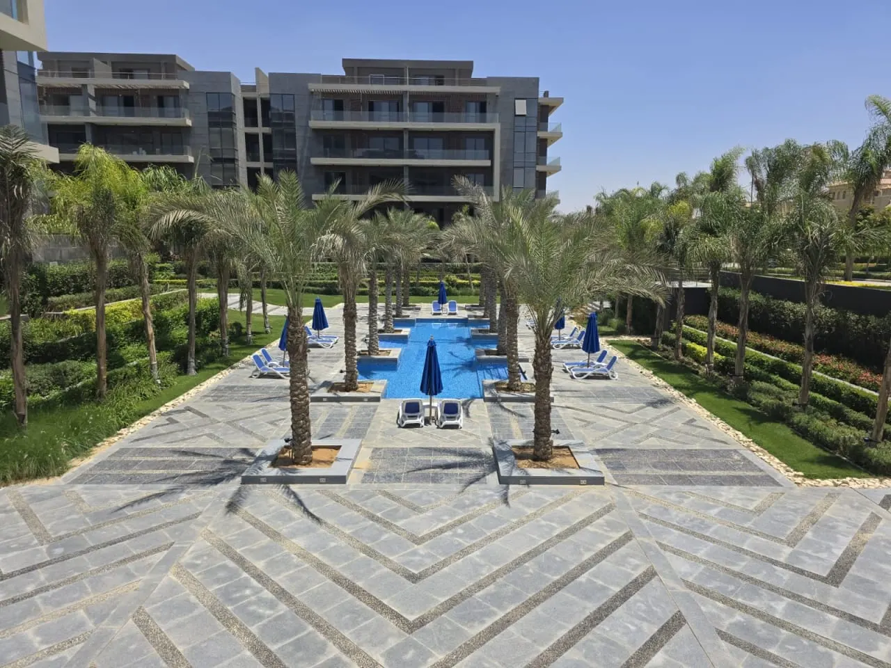 Palm-lined pool promenade between apartment blocks at Patio Oro, New Cairo, home to an apartment for sale