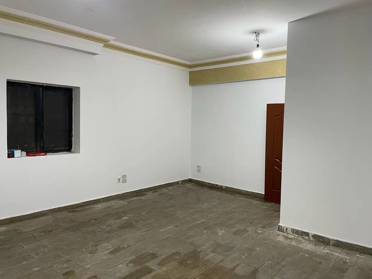 Empty room with white walls, tiled floor and a wooden door in a 133 m² ground floor for rent in New Cairo