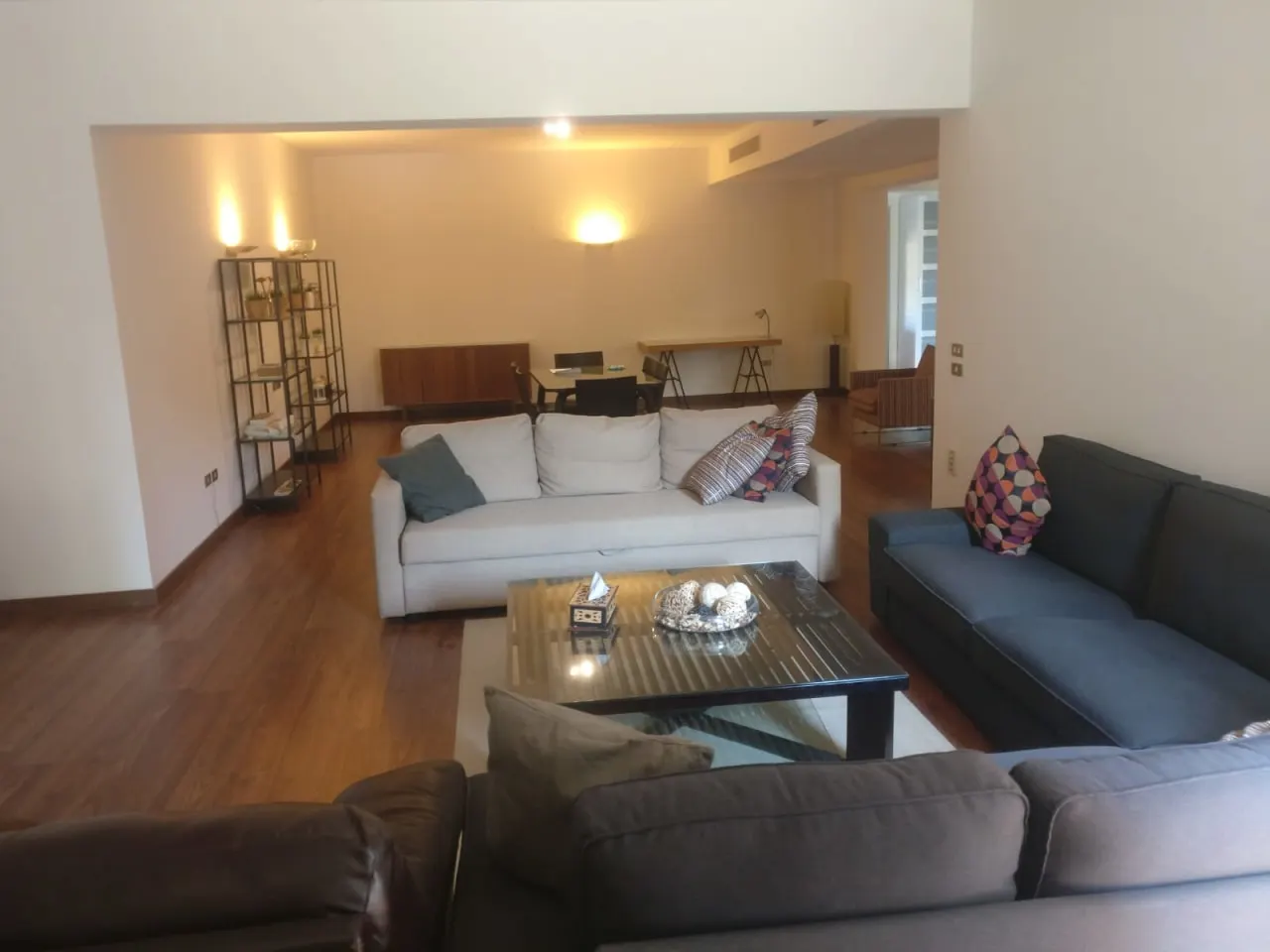 Living room with a white sofa, grey sectional and wood floors in a ground floor for rent in Fifth Settlement, New Cairo