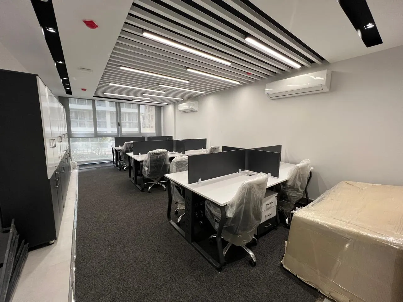 Open-plan office with white desks, black partitions and linear ceiling lights on a ground floor in New Cairo