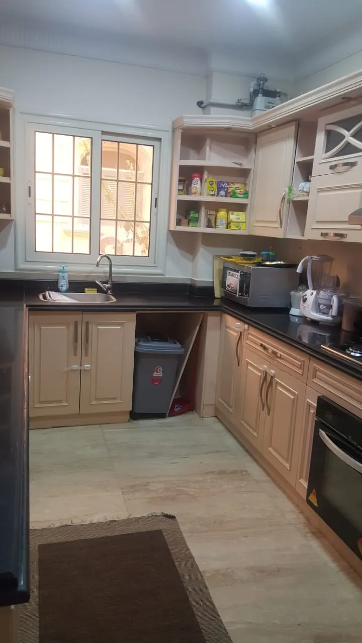 Kitchen with cream cabinets, black counters and a window in a three-bedroom ground floor for rent in West Golf, New Cairo