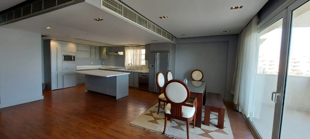 Open kitchen with an island and a dining table by the terrace doors in a penthouse in New Cairo