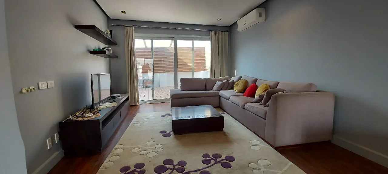 Living room with a corner sofa and glass doors onto the roof terrace of a penthouse in New Cairo