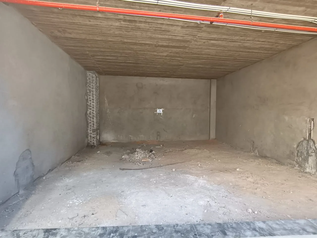 Deep core-and-shell shop interior with concrete walls and a sprinkler line in a 100 m² shop for rent in New Cairo
