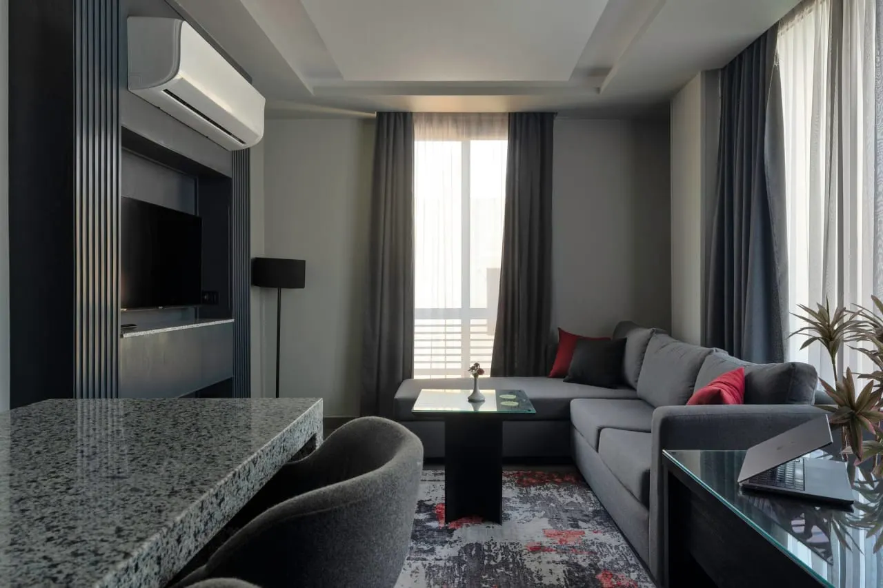 Living room with a grey sofa, red cushions and a TV wall in a one-bedroom serviced apartment in New Cairo