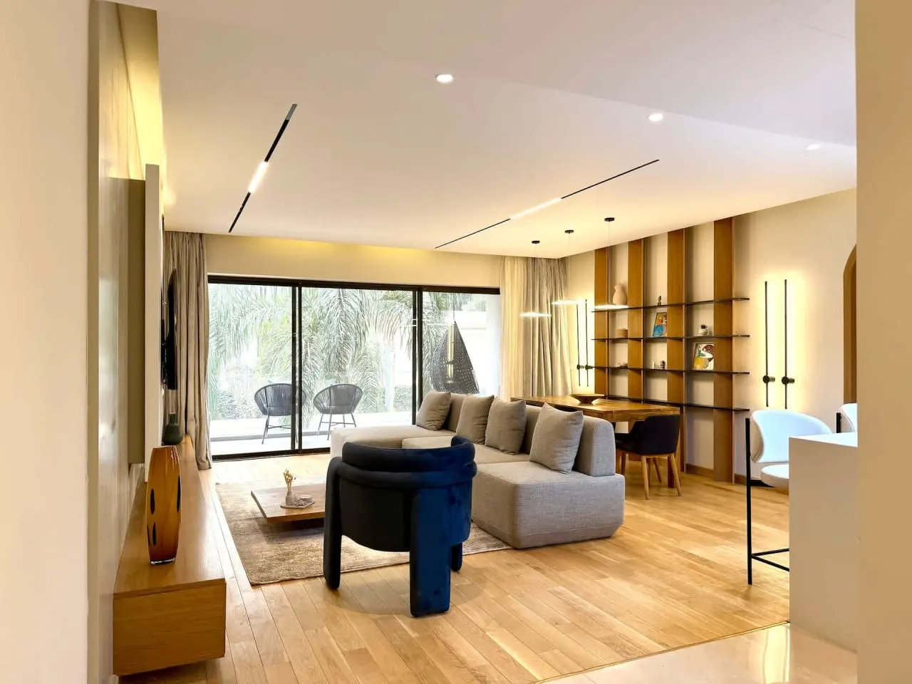 Open living room with grey sofas, wood shelving and garden-facing windows in a serviced apartment in New Cairo