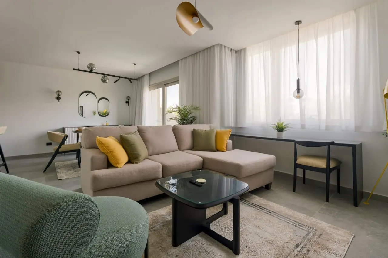 Furnished living room with a beige corner sofa and yellow cushions in a three-bedroom serviced apartment in New Cairo