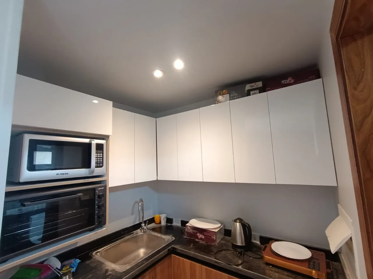 Kitchenette with white cabinets, a microwave, an oven and a sink in a furnished studio in New Cairo