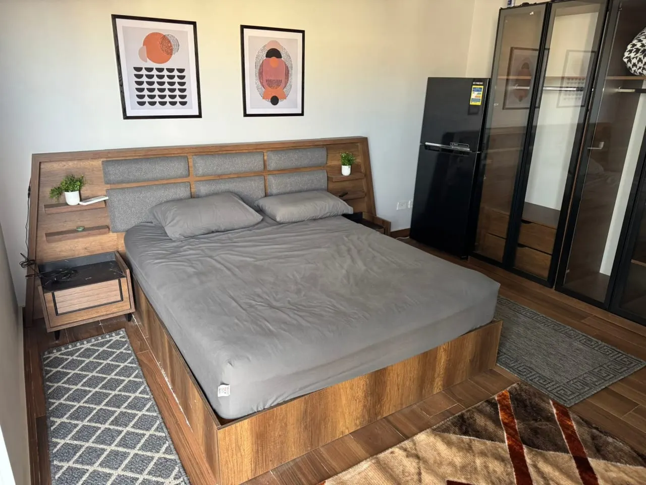 Bedroom with a wooden bed, grey linen and a glass wardrobe in a furnished studio for rent in New Cairo