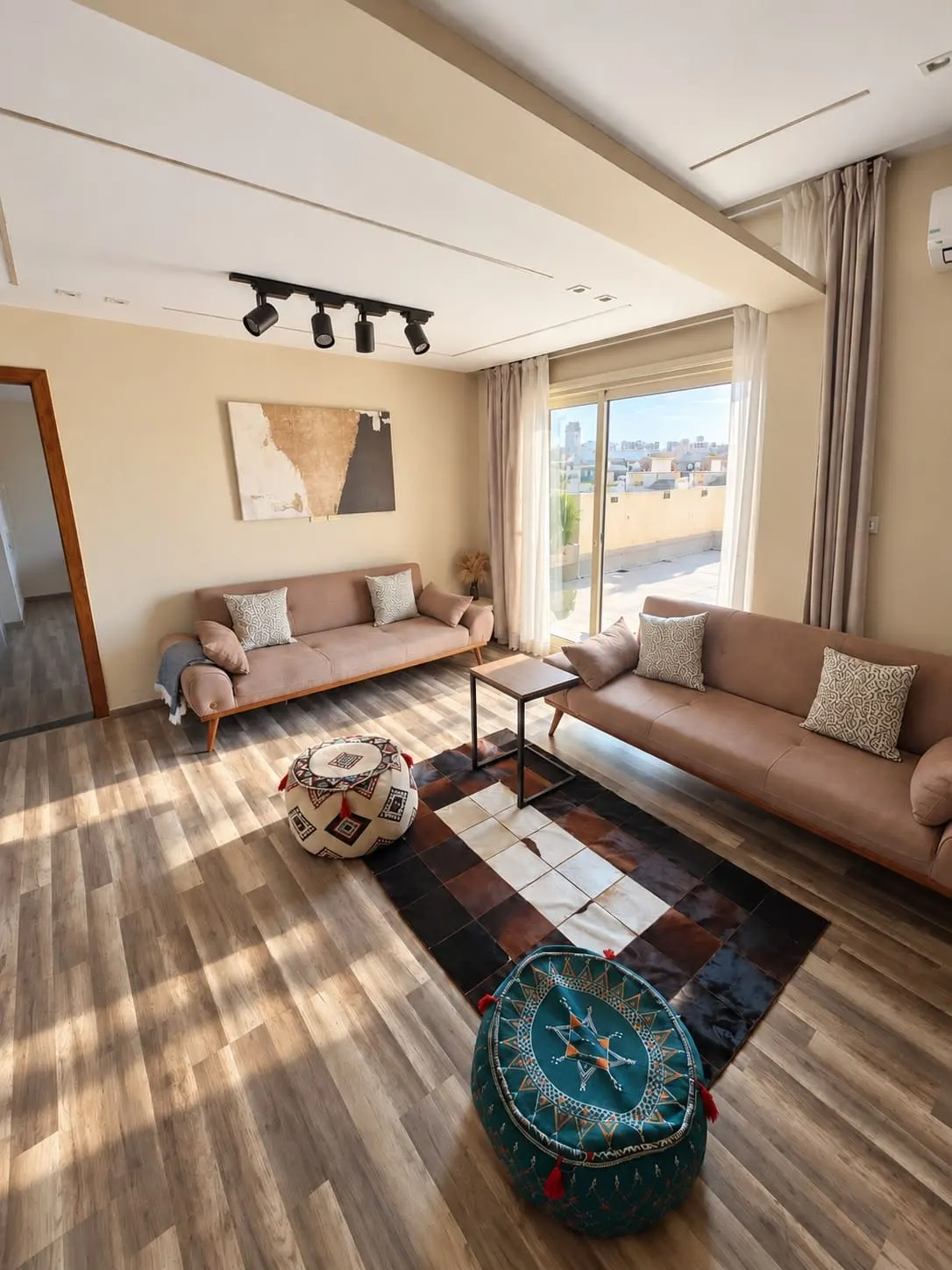 Living room with two beige sofas, wood floors and a wide window in a studio for rent in New Cairo