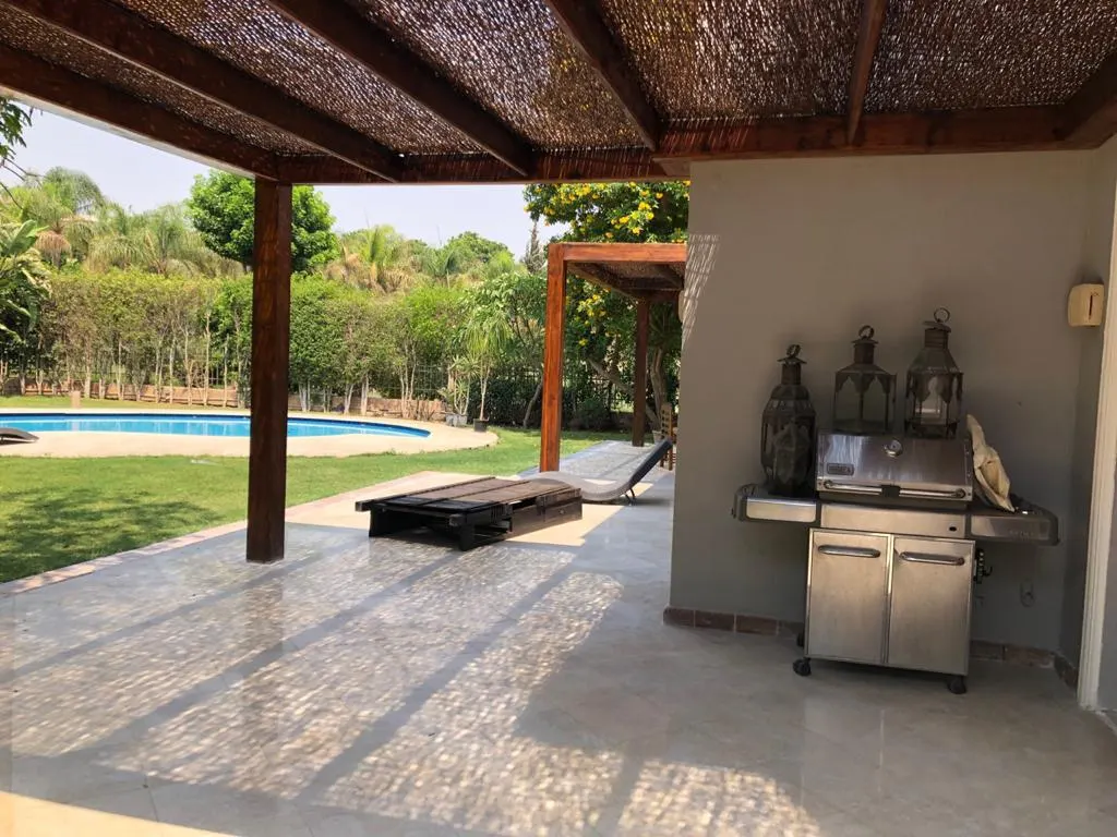 Covered terrace with a barbecue grill overlooking a lawn and swimming pool at a villa in Fifth Settlement, New Cairo