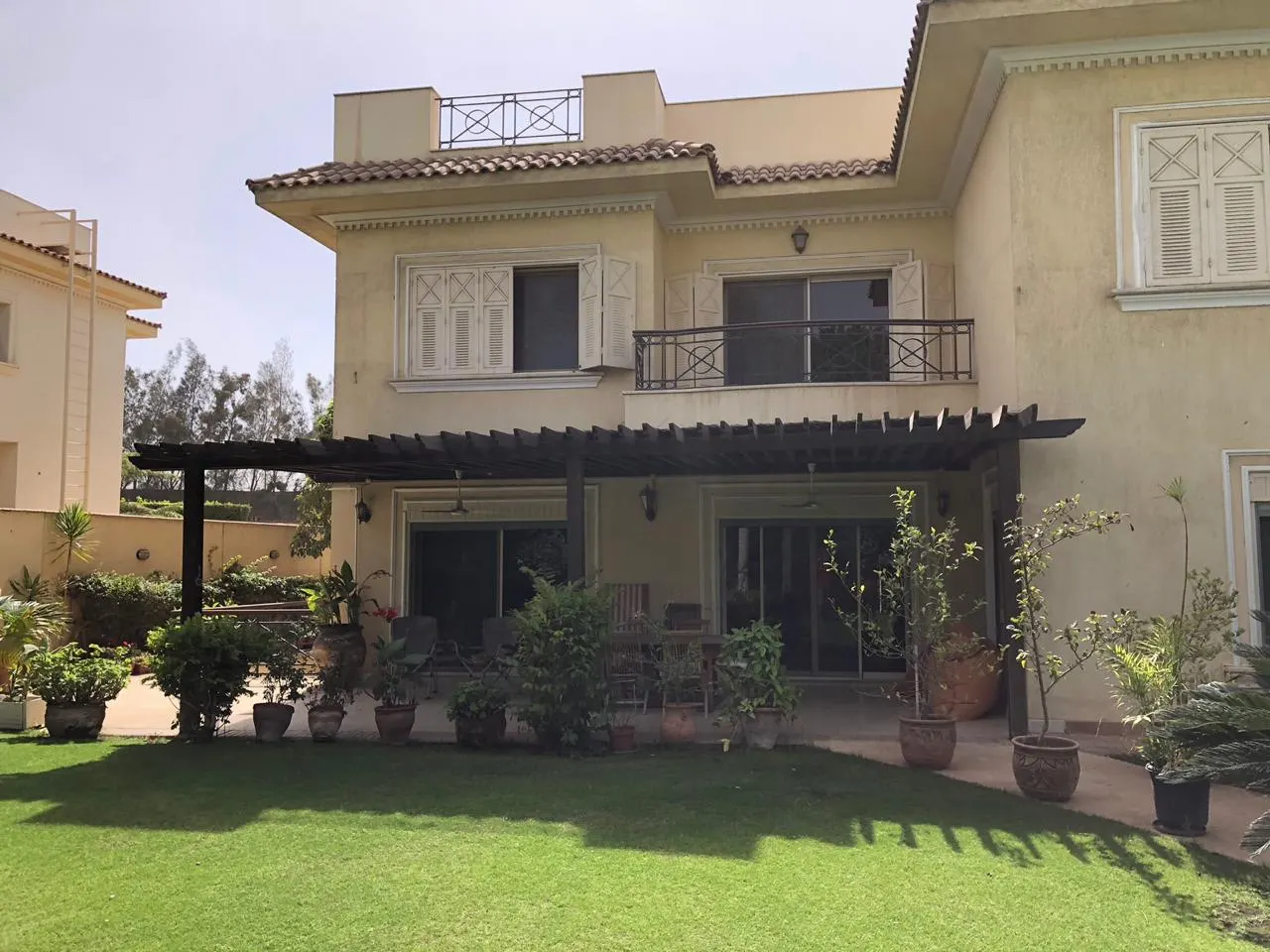 Rear of a villa with a pergola, potted plants and a lawn in Katameya, New Cairo