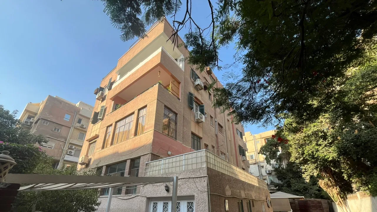 عمارة سكنية بلون ترابي فوق جراجاتها الخاصة تحيط بها الأشجار في أحد شوارع السرايات
