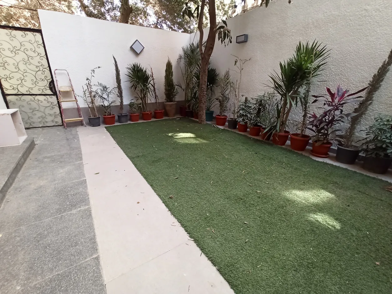 حديقة خاصة مسوّرة بها نجيل ونباتات في أصص أمام شقة دور أرضي في سرايات المعادي
