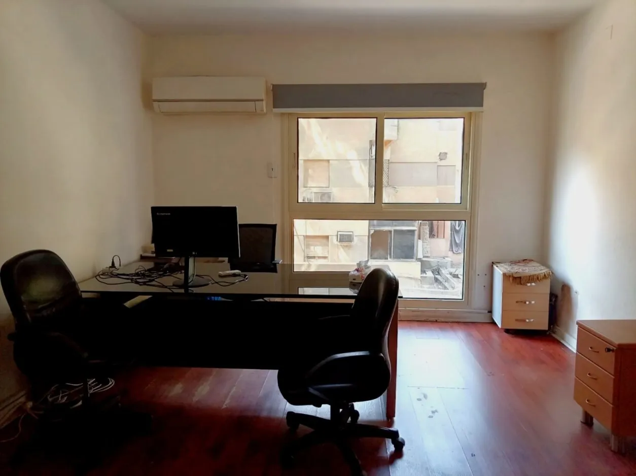 مساحة عمل مفتوحة تحت فتحة سقف زجاجية كبيرة، مع غرف بجدران زجاجية وباب على فناء مزروع، في مكتب بسرايات المعادي