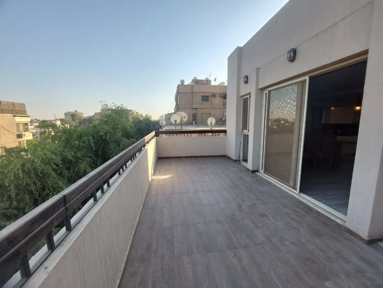 غرفة معيشة مفروشة بنوافذ من الأرض للسقف تطل على تراس ومنظر المدينة في بنتهاوس بسرايات المعادي