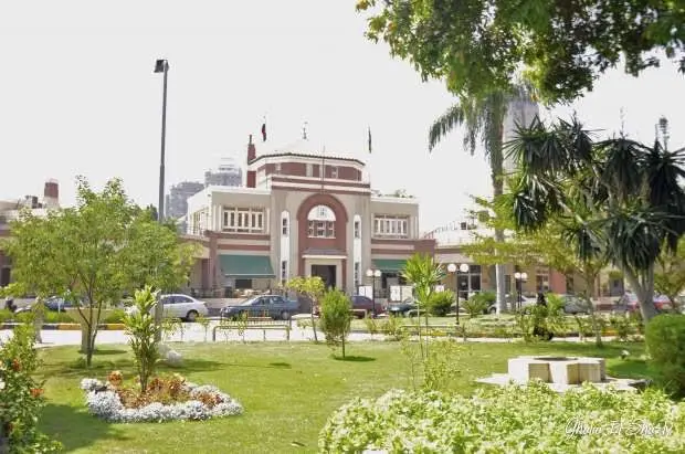 A historic building with arched windows behind landscaped lawns, flower beds and palm trees in Zamalek