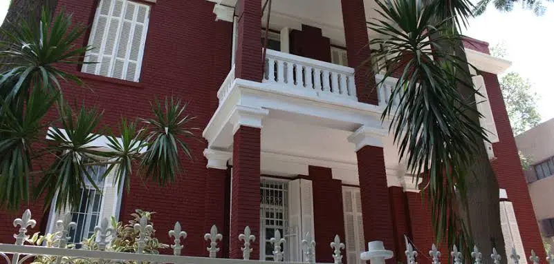 فيلا تاريخية من الطوب الأحمر بدرابزين أبيض وأشجار نخيل في شارع سكني بالزمالك