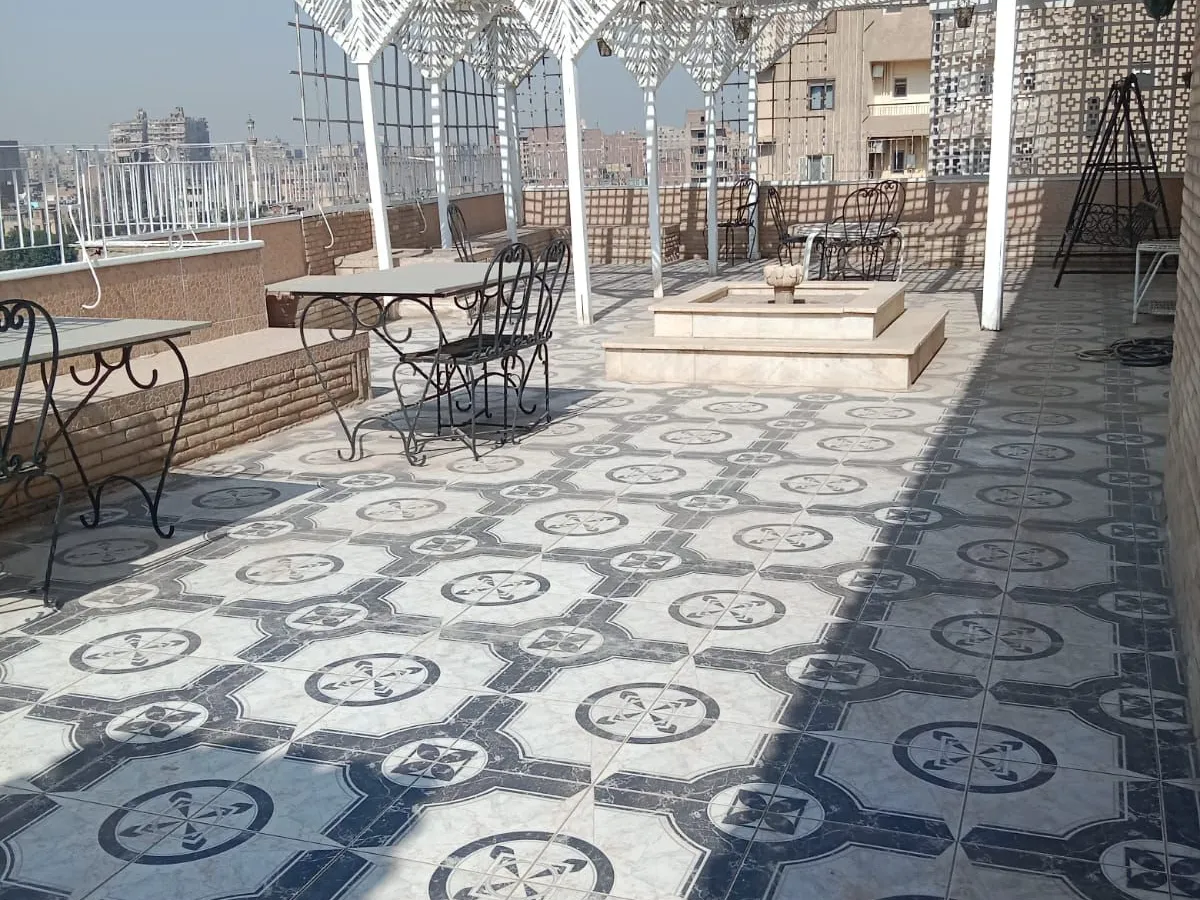 تراس على السطح بأرضية منقوشة وبرجولة بيضاء وطاولات صغيرة وإطلالة على المدينة من دوبلكس في الزمالك
