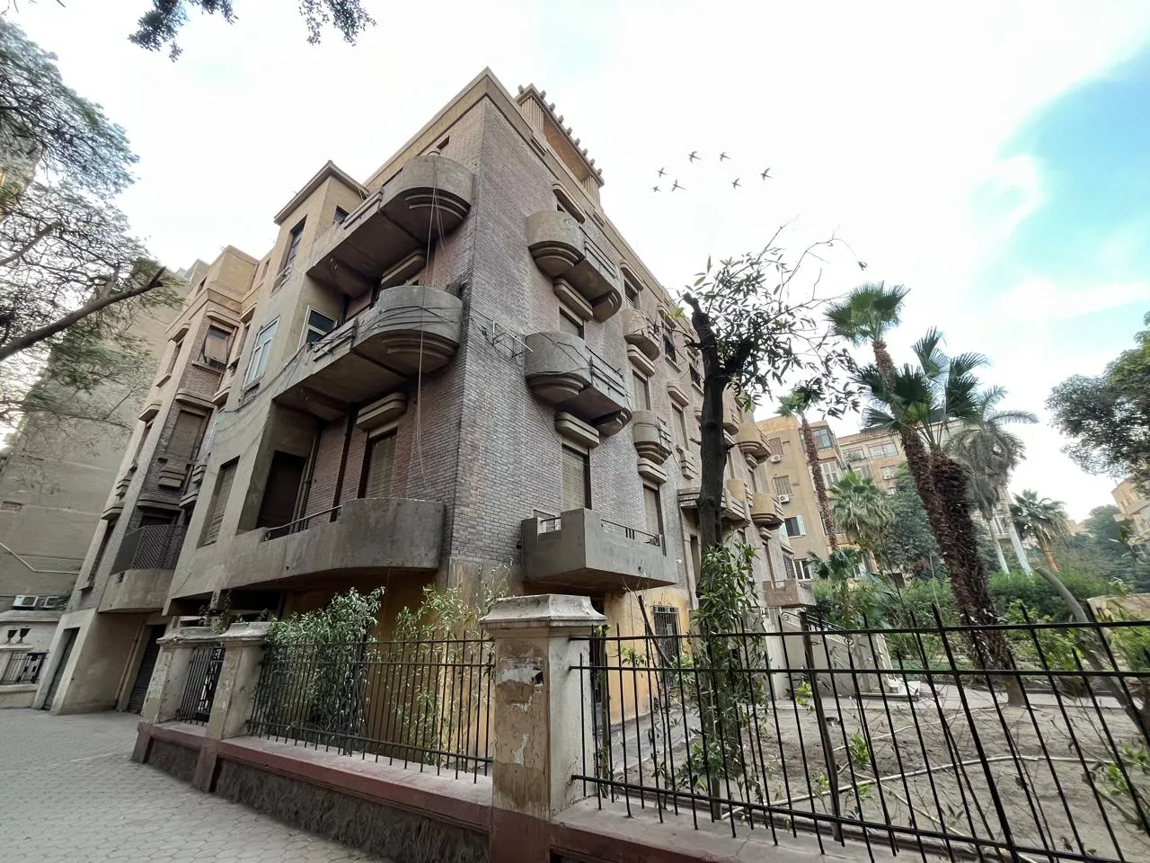 فيلا من الطوب متعددة الأدوار بشرفات مستديرة خلف سور حديدي ونخيل في جنوب الزمالك