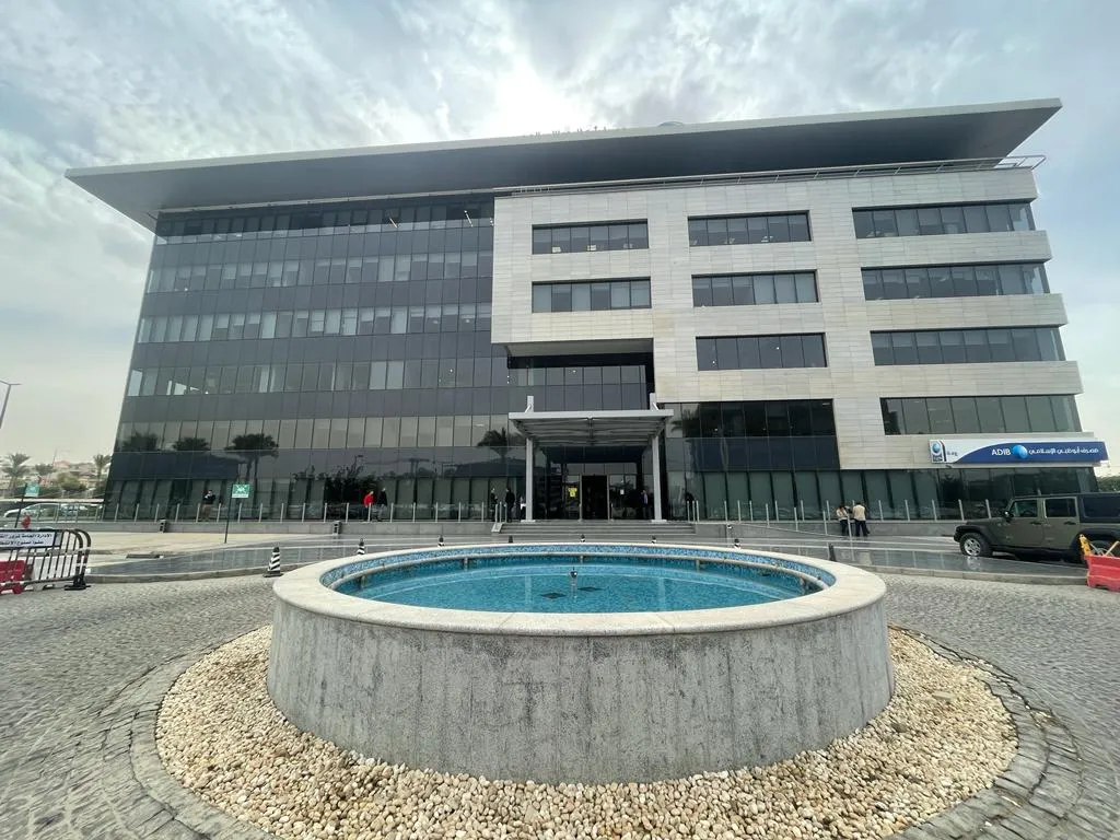 Glass and stone administrative building with a round fountain in its forecourt in New Cairo, Cairo