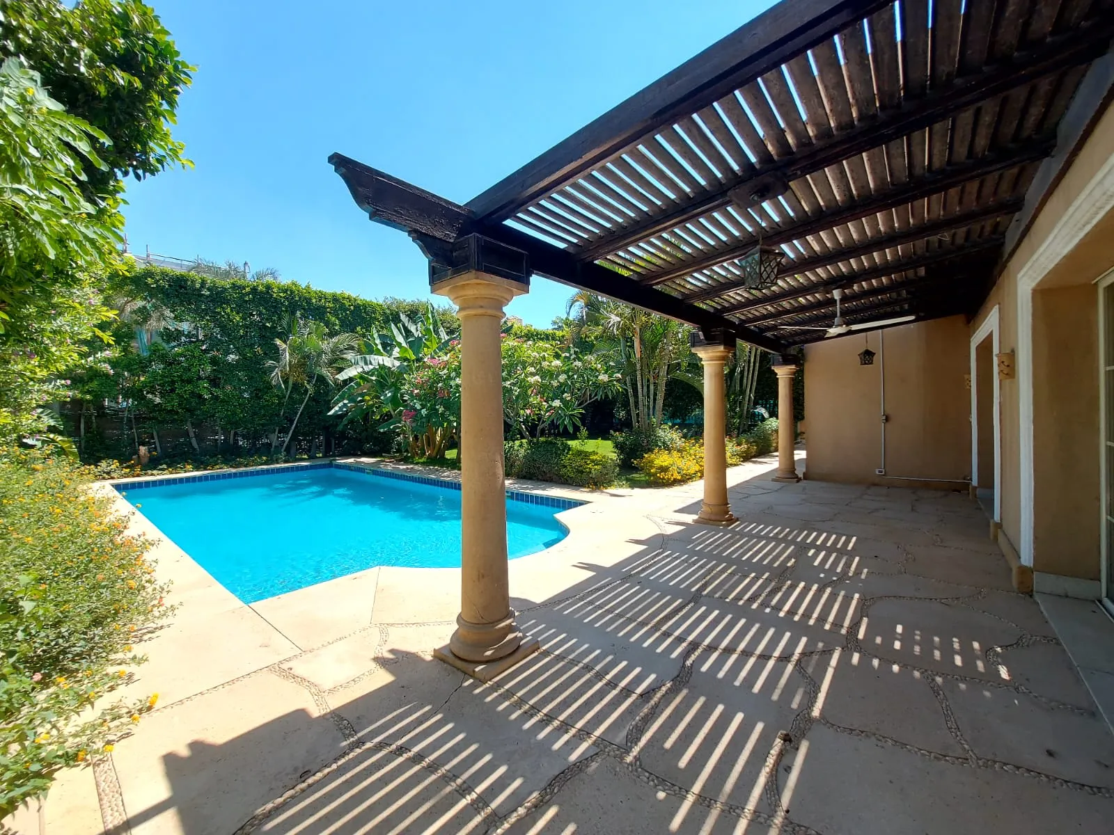 Pergola-shaded patio beside a swimming pool and tropical garden at a villa in Fifth Settlement, New Cairo